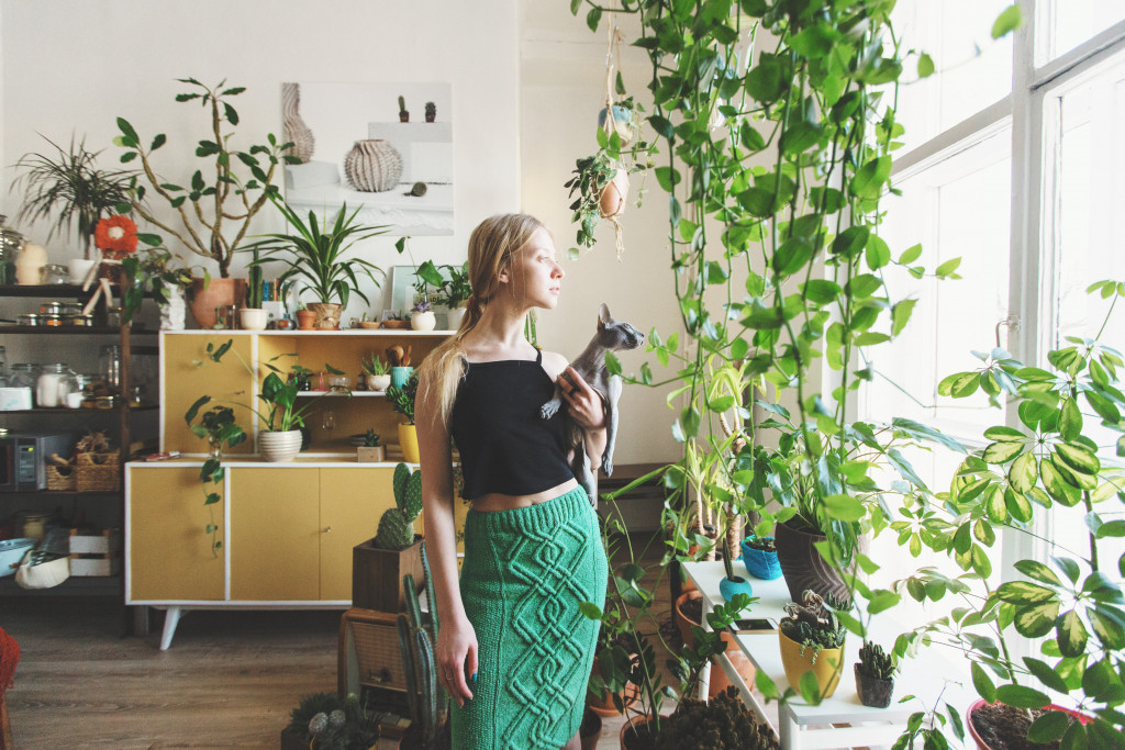 a lady holding a cat inside a house full of indoor plants